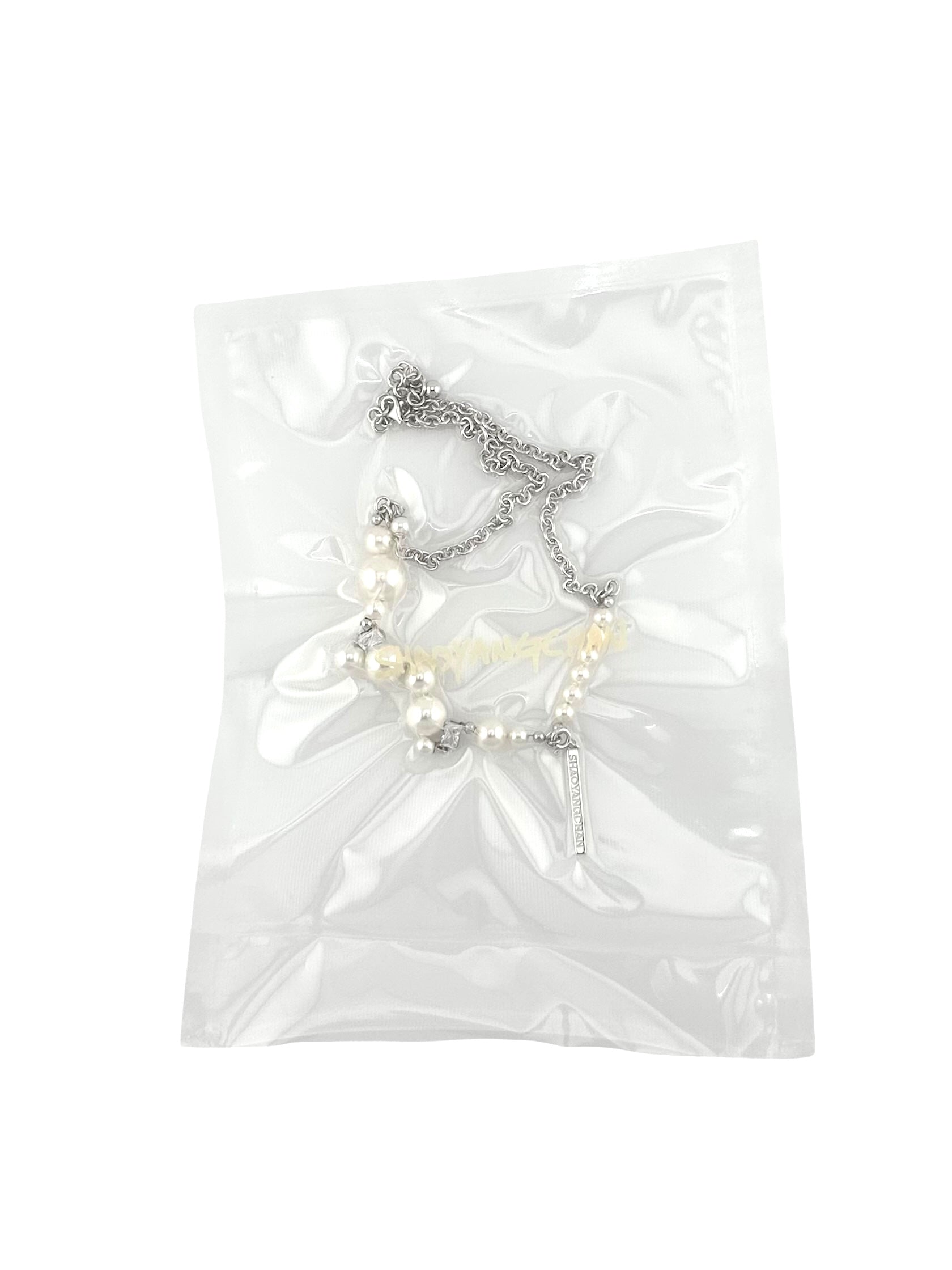 A clear plastic bag containing a pearls silver necklace.